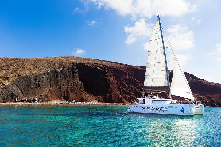Sailing catamaran off the Red Beach cliffs on a premium small-group Santorini catamaran cruise, Santorini Greece